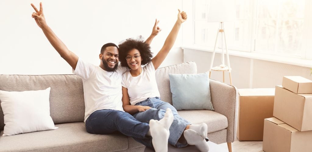 Excited Black Family Couple Celebrating Moving New House Sitting Indoors