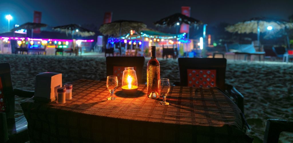 Night view of beach party in a beach cafe with a bottle of rose wine and glasses on the table. 