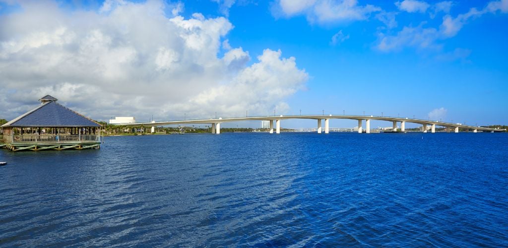 A long river bridge, blue water, and a cabin on the side. 