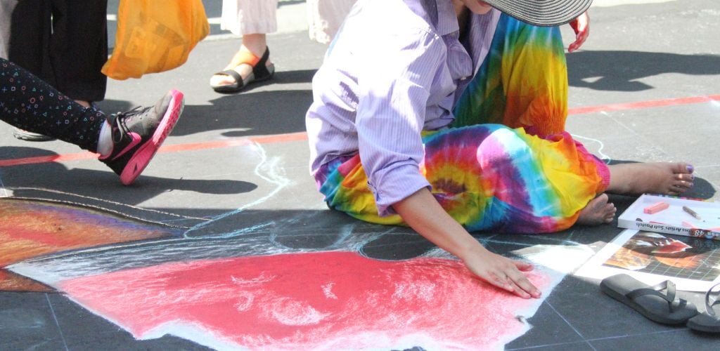 A woman creates art on the street's floor. 
