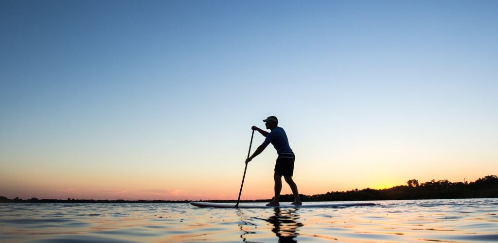 Silhouette of a man standing up on a paddleboard. 