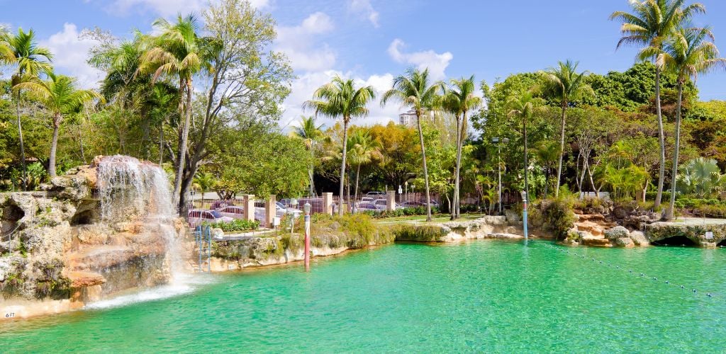 The public swimming pool with mini falls known as the Venetian Pool surrounded by green trees and plants.