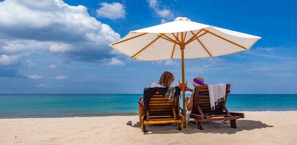 Beach summer couple on island vacation holiday relax in the sun in their deck chairs. 