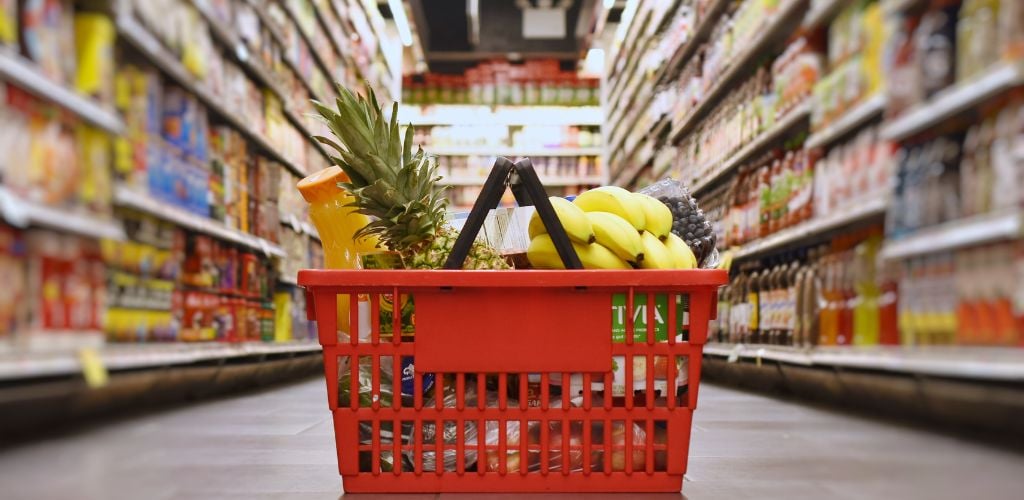 There is a red bucket filled with fruits near the center aisle of the grocery store.