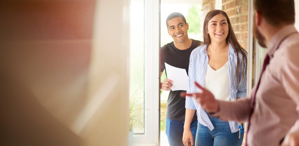 A young couple views a property guided by the home owner. they standing in the hallway of the house and chatting about the house contract that they are holding. 