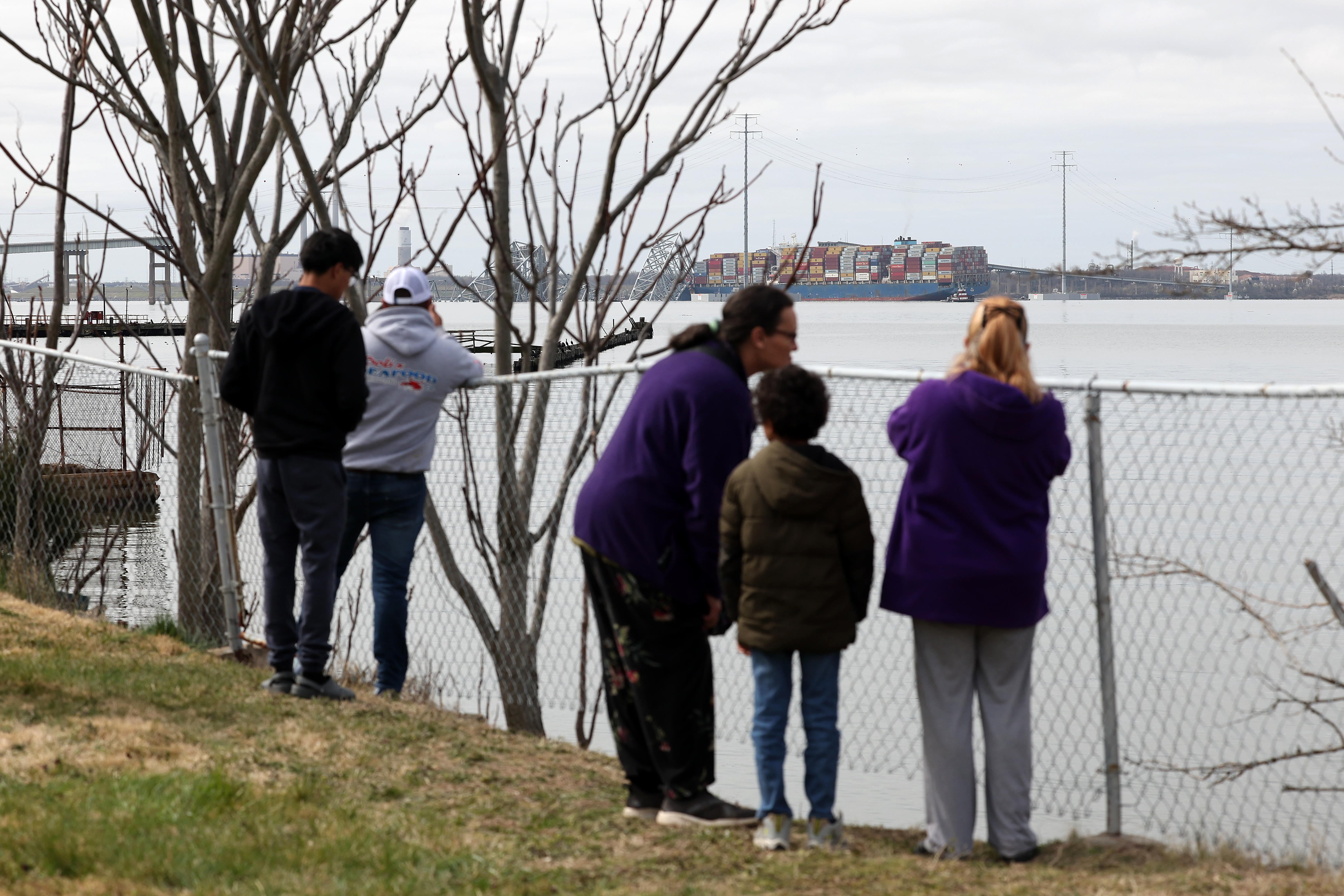 Residents look on after a cargo ship ran into and collapsed the Francis Scott Key Bridge on March 26, 2024 in Baltimore. Conspiracy theorists online quickly spread narratives to millions online that the accident was part of a nefarious scheme.