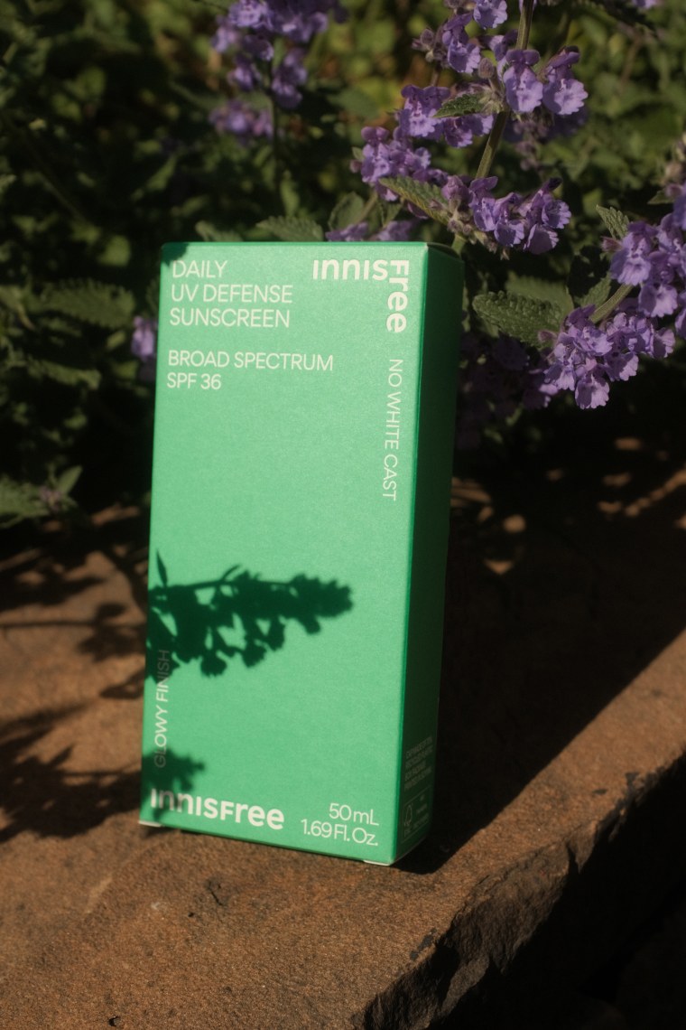 A box containing a bottle of sunscreen amidst purple flowers and leaves.