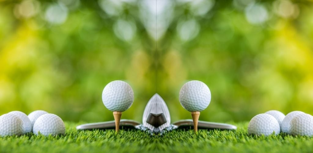 mirror image of golf ball on tee ready to practice, more golf balls on lawn to side of tee