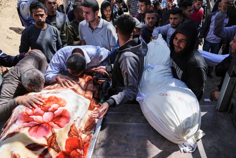 A crowd mourns over wrapped bodies