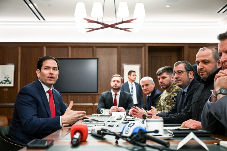 Marco Rubio, left, sits across a table with many people on the other side