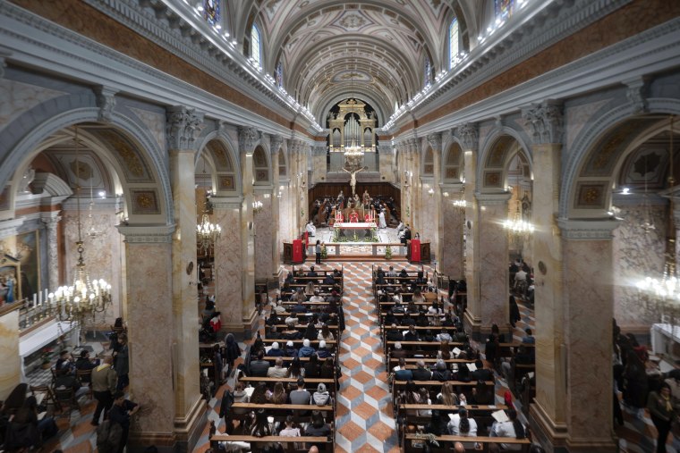 A wide view of the interior of an ornate church, people sitting in the pews and at the altar