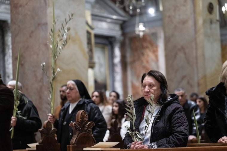 People sit in pews and hold palm leaves