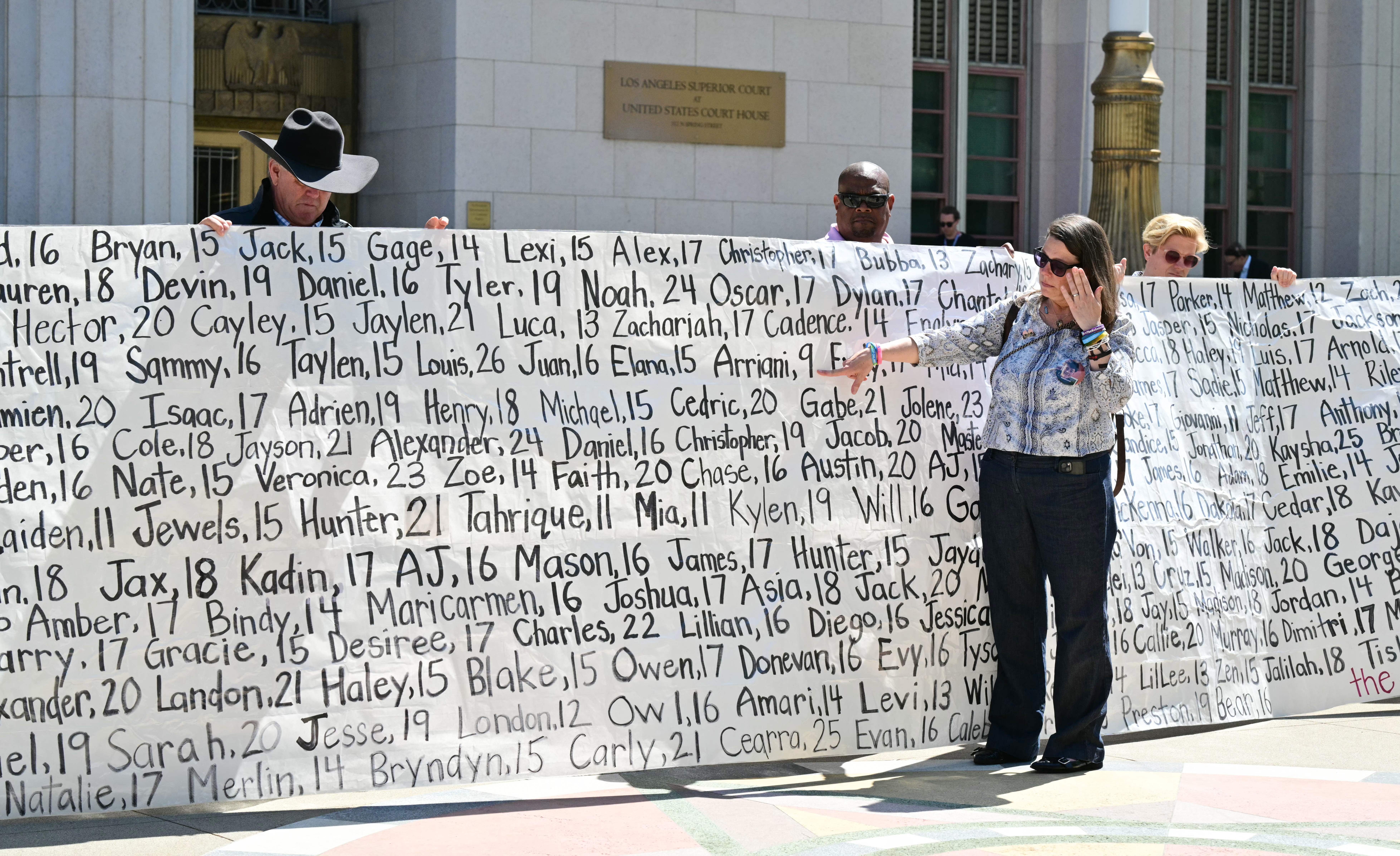 Mary Rodee, whose 15-year-old son died by suicide, points to a banner listing victims
