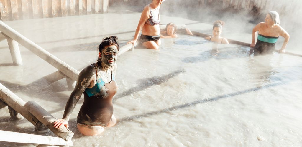 A group of women bathed in the mud pool, and the woman facing the camera was covered in mud on her face and arms.