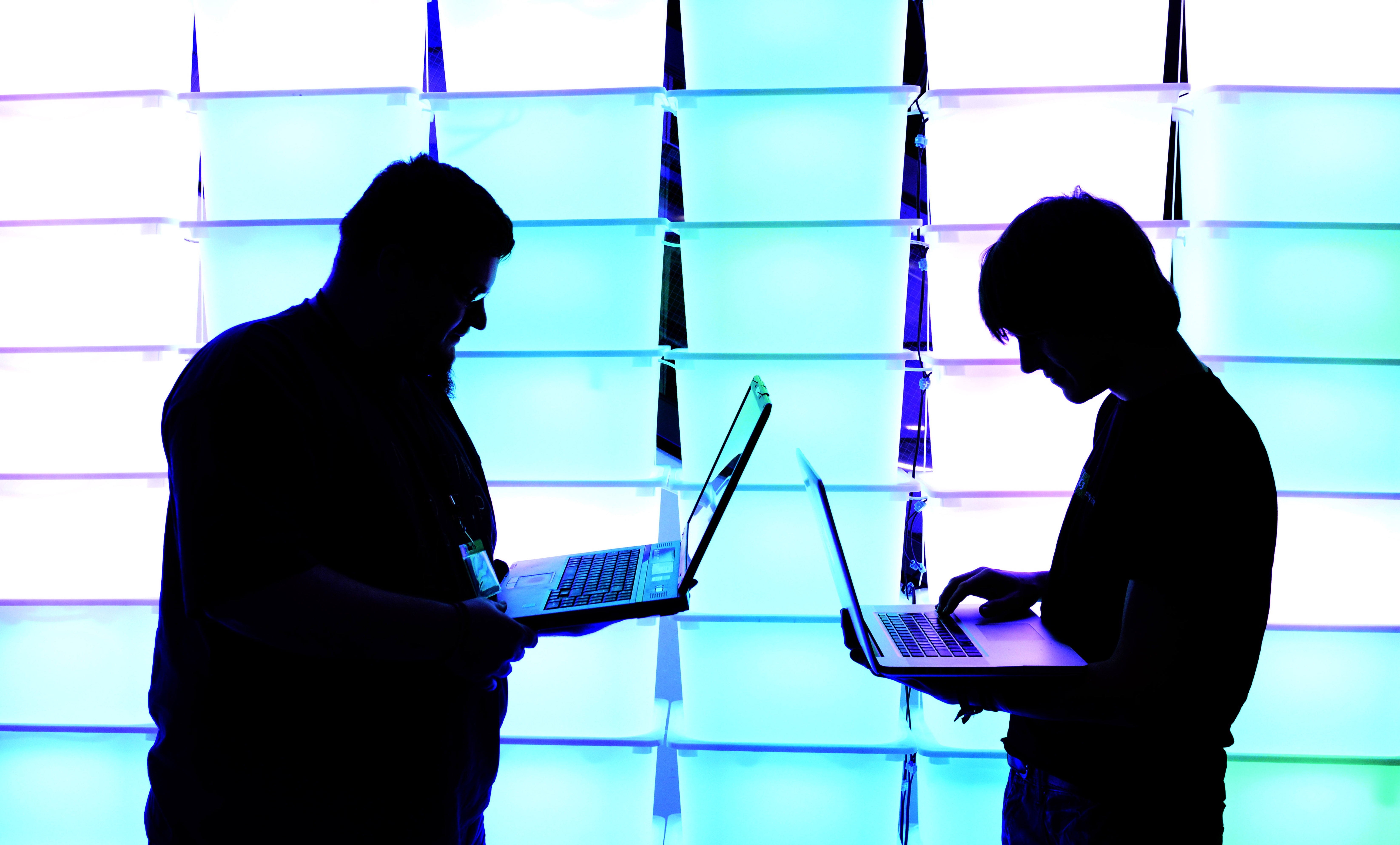 Participants hold their laptops in front of an illuminated wall at the annual Chaos Computer Club (CCC) computer hackers