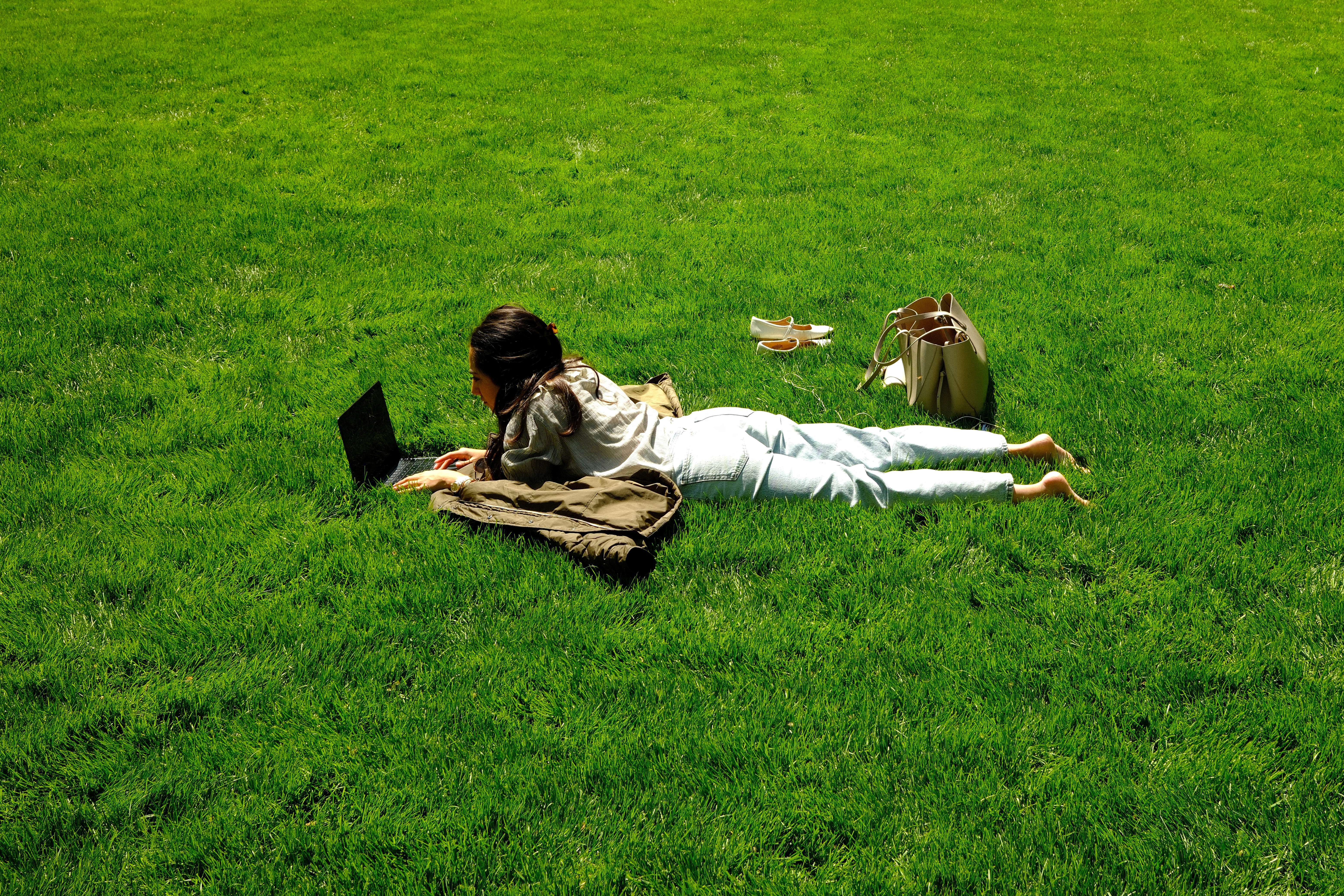 A woman uses a laptop as she lies on the grass in a park in the Manhattan borough of New York City on April 24, 2026.