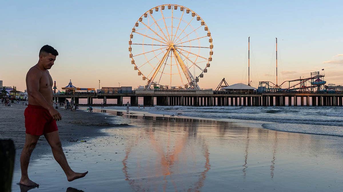 A man walks past a Ferris wheel's reflection on the beach at sunset in Atlantic City, New Jersey.
